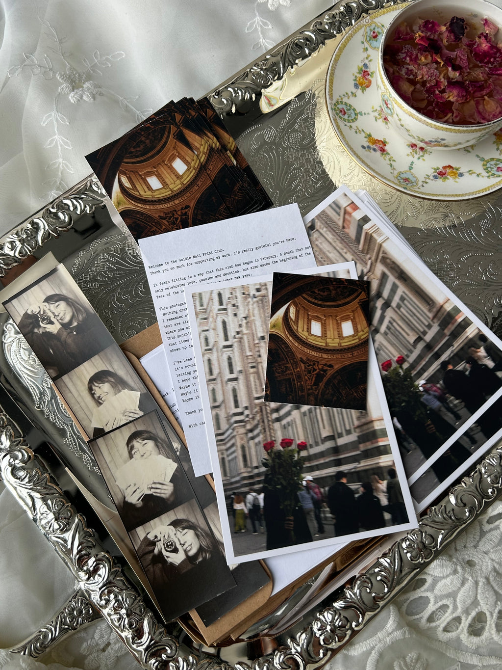 Collection of vintage photographs and postcards on a decorative tray with a teacup and saucer.
